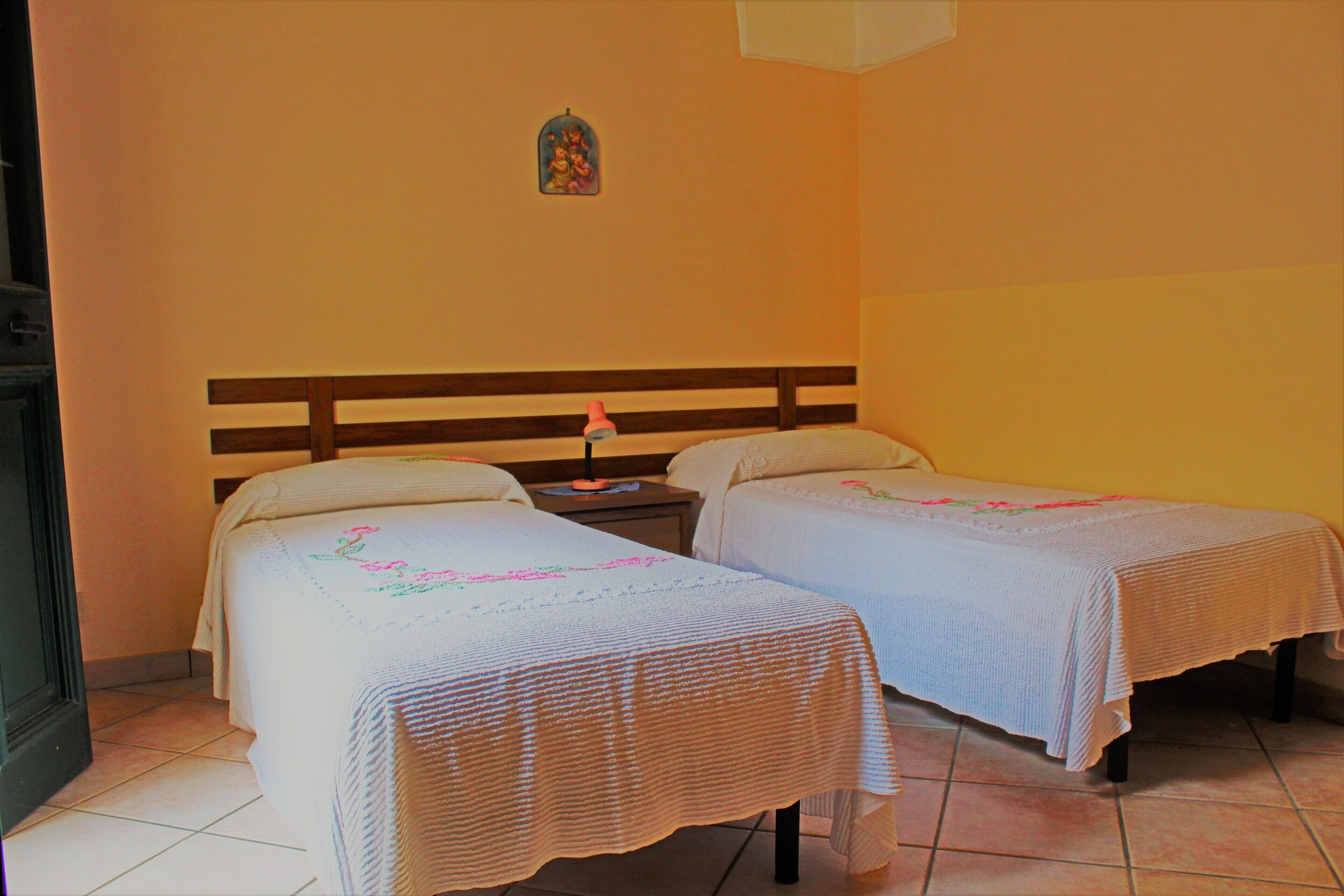 A room with two beds, a nightstand with a lamp, and a small decorative item on the wall.