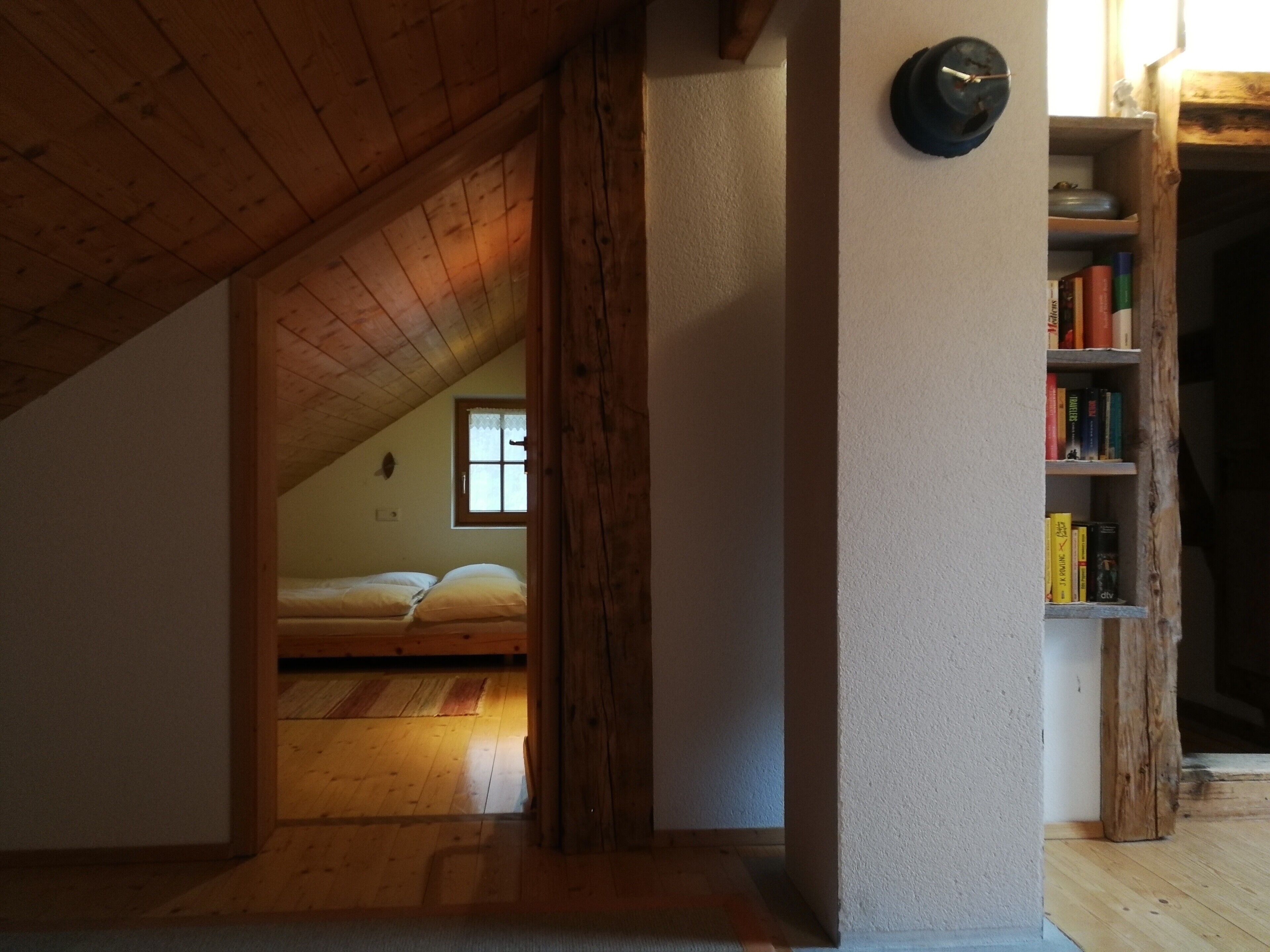 A room with a sloped ceiling, a wooden bookshelf, and a bed with a window.