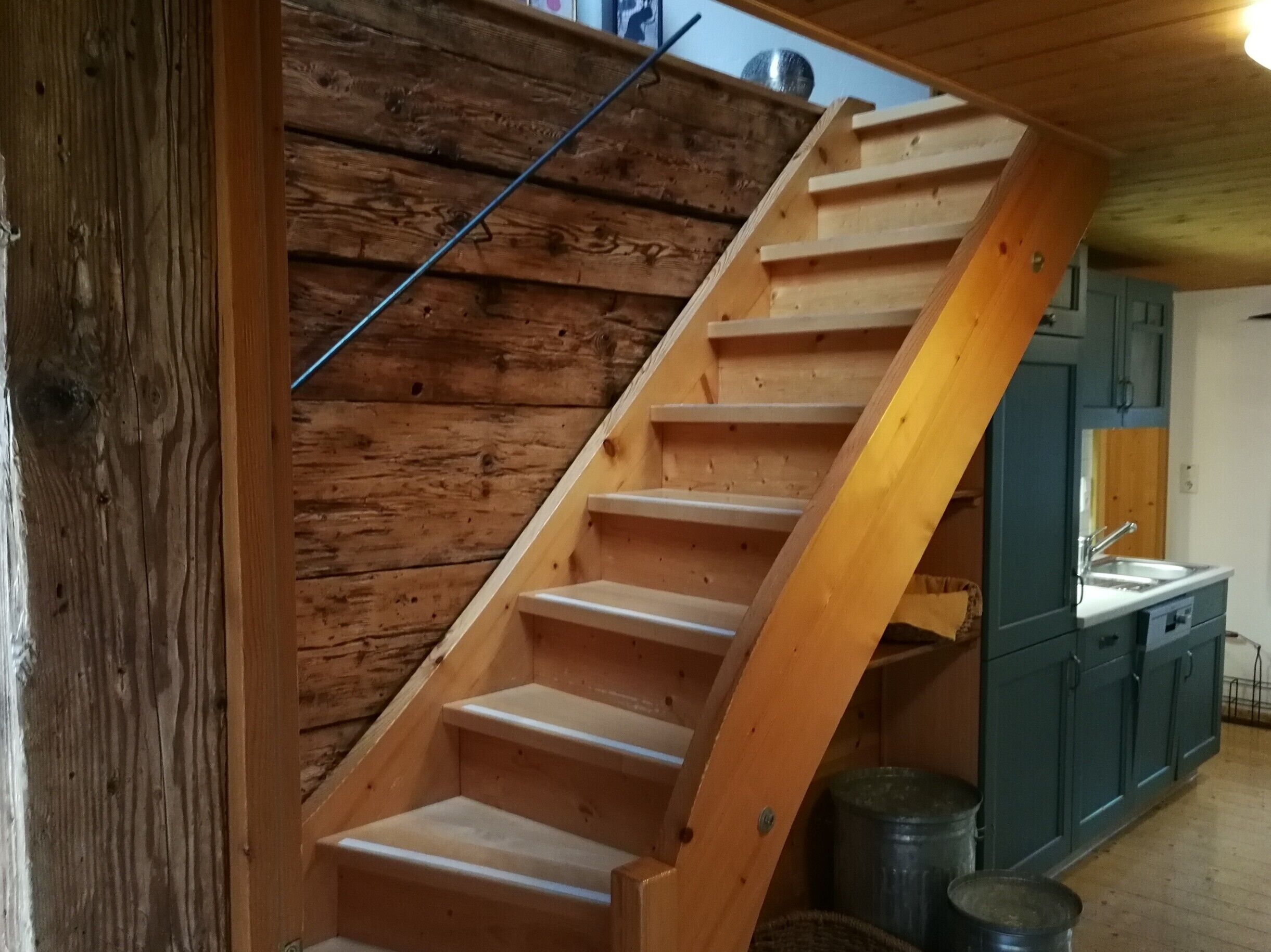 Eine Holztreppe führt zu einer Küche mit Spüle und Schränken.