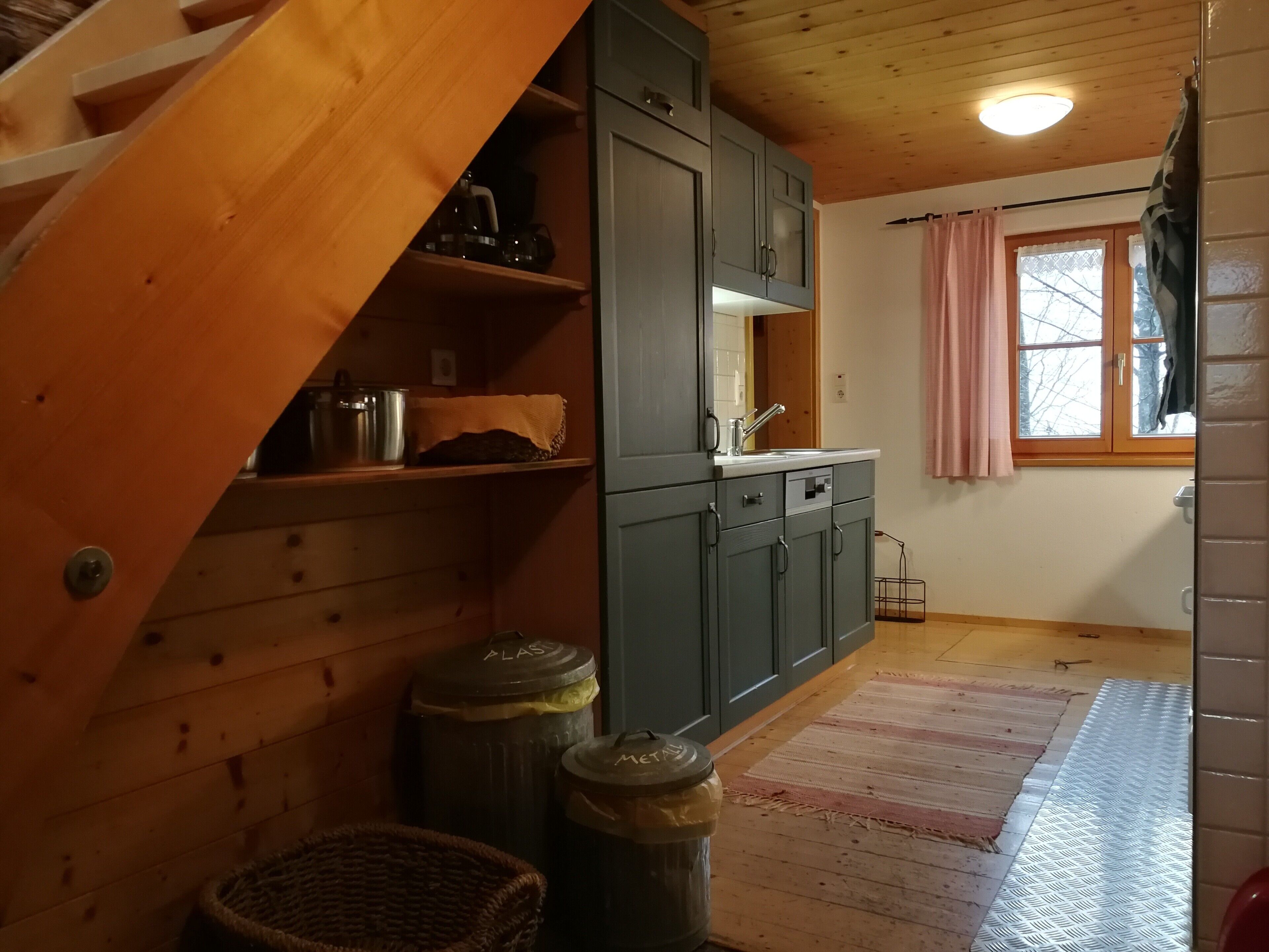 Un intérieur en bois comprenant un espace cuisine, avec des placards, un évier et une fenêtre avec des rideaux.