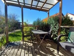 Una terraza de madera con pérgola, una mesa y dos sillas.