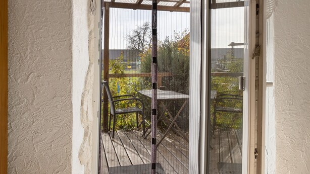 Een afgesloten terras met een tafel en stoelen, een houten terras en uitzicht op bomen en een hek.