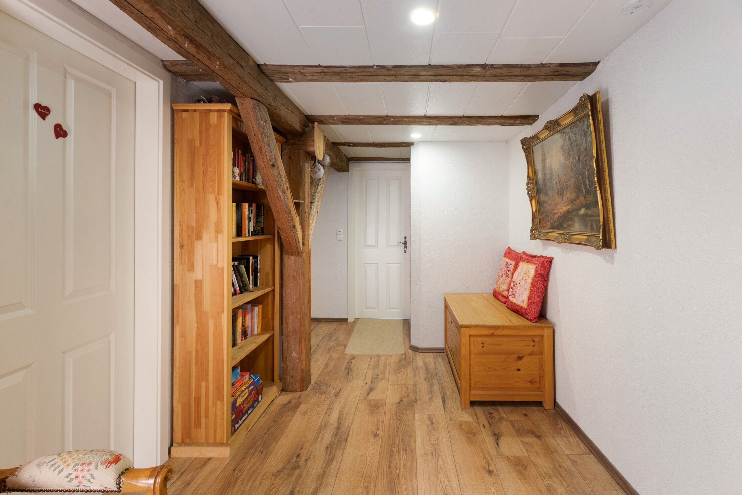 Un pasillo con estanterías de madera, un banco, una puerta y un cuadro en la pared.