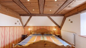 Un dormitorio con techo de madera, una cama con colcha a rayas, dos mesitas de noche y un radiador.