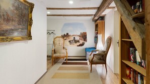 Una habitación con techo de madera, un mural, una estantería y dos sillas.