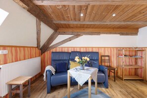 Une pièce avec un plafond en bois, un canapé bleu, une petite table sur laquelle est posé un vase de fleurs et une bibliothèque.