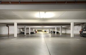 Un parking intérieur avec des piliers blancs, un sol en béton et une allée centrale.