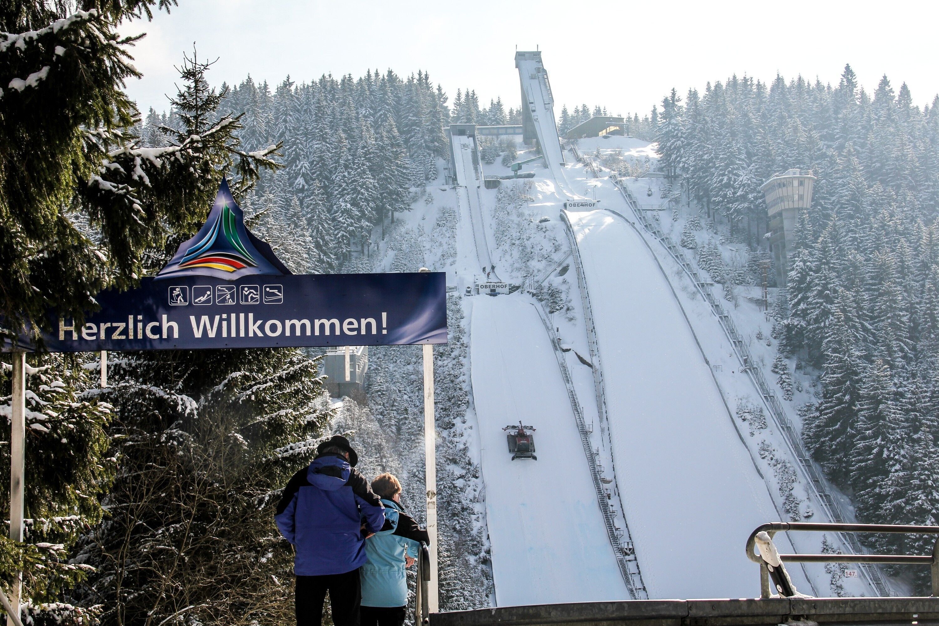 A ski lift with a sign reading 'Herzlich Willkommen!' and a snowy forest in the background.