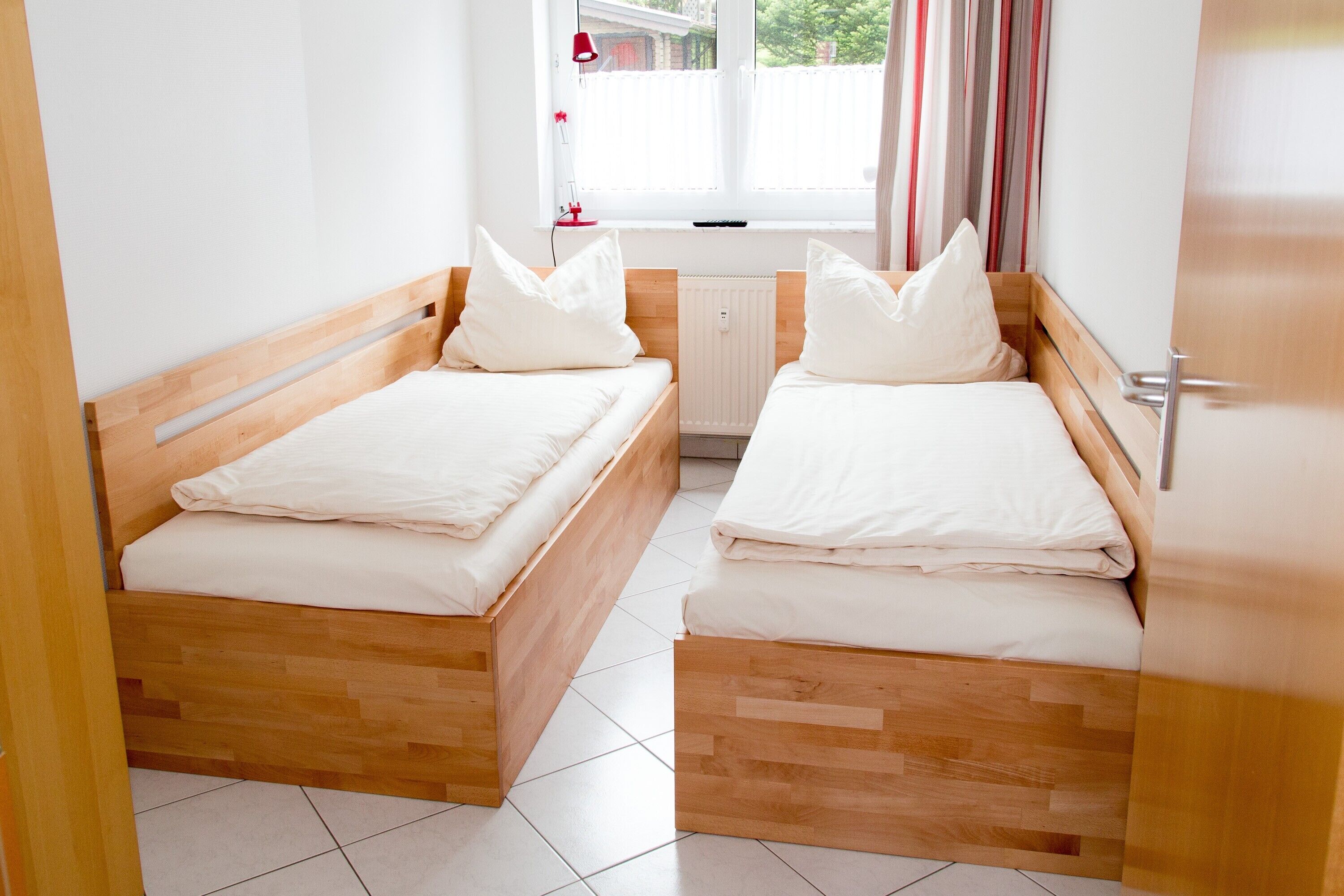 Una habitación con dos camas de madera, ropa de cama blanca, una ventana con cortinas y un radiador.