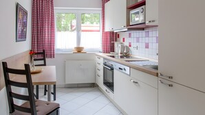 Eine Küche mit weißen Schränken, einer Mikrowelle, einem Wasserkocher und einem Fenster mit roten Vorhängen.