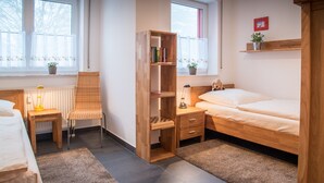 A room with a bed, a chair, a wooden bookshelf, a desk, and a window with curtains. - Apartment 'Ferienwohnung Tannenblick 3-4' with Mountain View, Balcony and Wi-Fi (Oberhof)