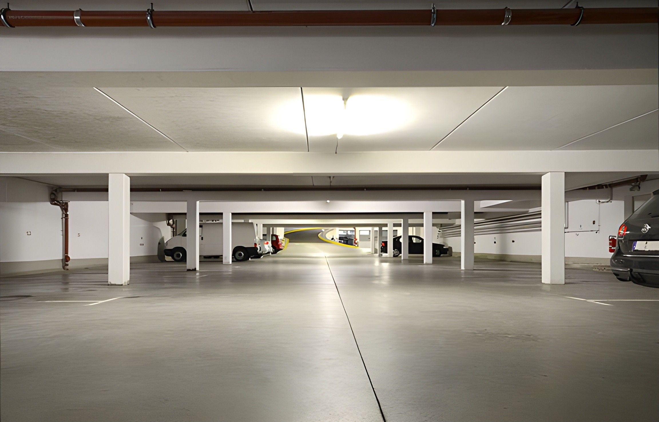 En indendørs parkeringskælder med hvide søjler, beton gulve og en midterste gang.