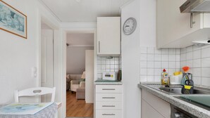 Una cucina con mobili bianchi, un orologio, un fornello e un'area pranzo con tavolo e sedie.