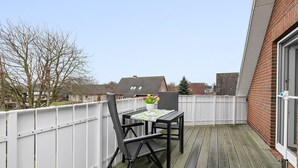 Un balcone con tavolo e sedie, un recinto bianco e vista su case sullo sfondo.