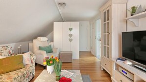 Un soggiorno con divano, poltrona, televisore, mobile contenitore e un vaso con fiori.