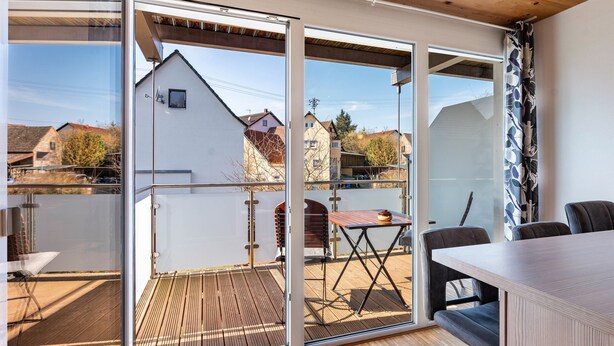 Ein modernes Zimmer mit einer großen Schiebeglasdoor zu einer Außenterrasse, einer Holzbalkendecke und einem Tisch mit Stühlen.