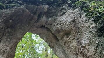 Eine Holztreppe führt zu einem natürlichen Felsbogen, der von Grün umgeben ist.