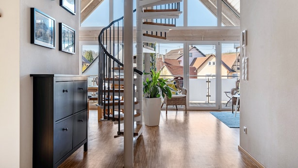 Un interior moderno con una escalera en espiral, suelo de madera, una planta en maceta y vistas al exterior.