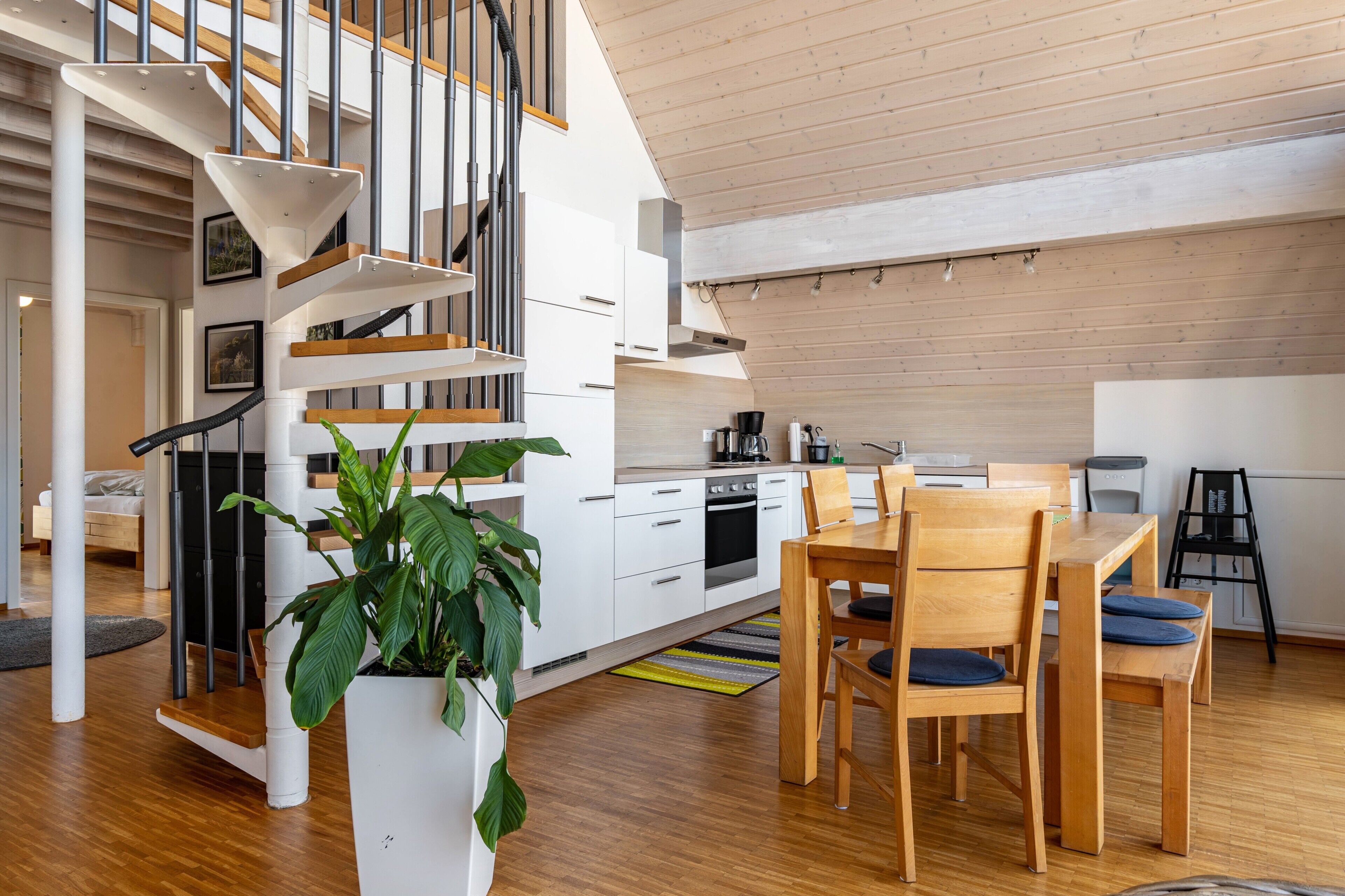 Una cucina moderna con mobili bianchi, un tavolo da pranzo in legno e una scala con ringhiera bianca.