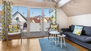 Una habitación con balcón, mobiliario de mimbre, un sofá gris y una mesita.