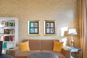 Un salon avec un canapé beige, une bibliothèque et des œuvres d’art encadrées accrochées au mur.