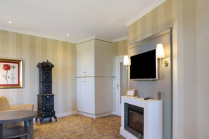 Quarto de hotel com lareira, televisão montada acima dela, relógio e um quadro na parede.