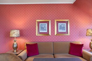 Une pièce avec un mur orné de motifs, deux tableaux encadrés, un canapé avec des coussins rouges et deux lampes.