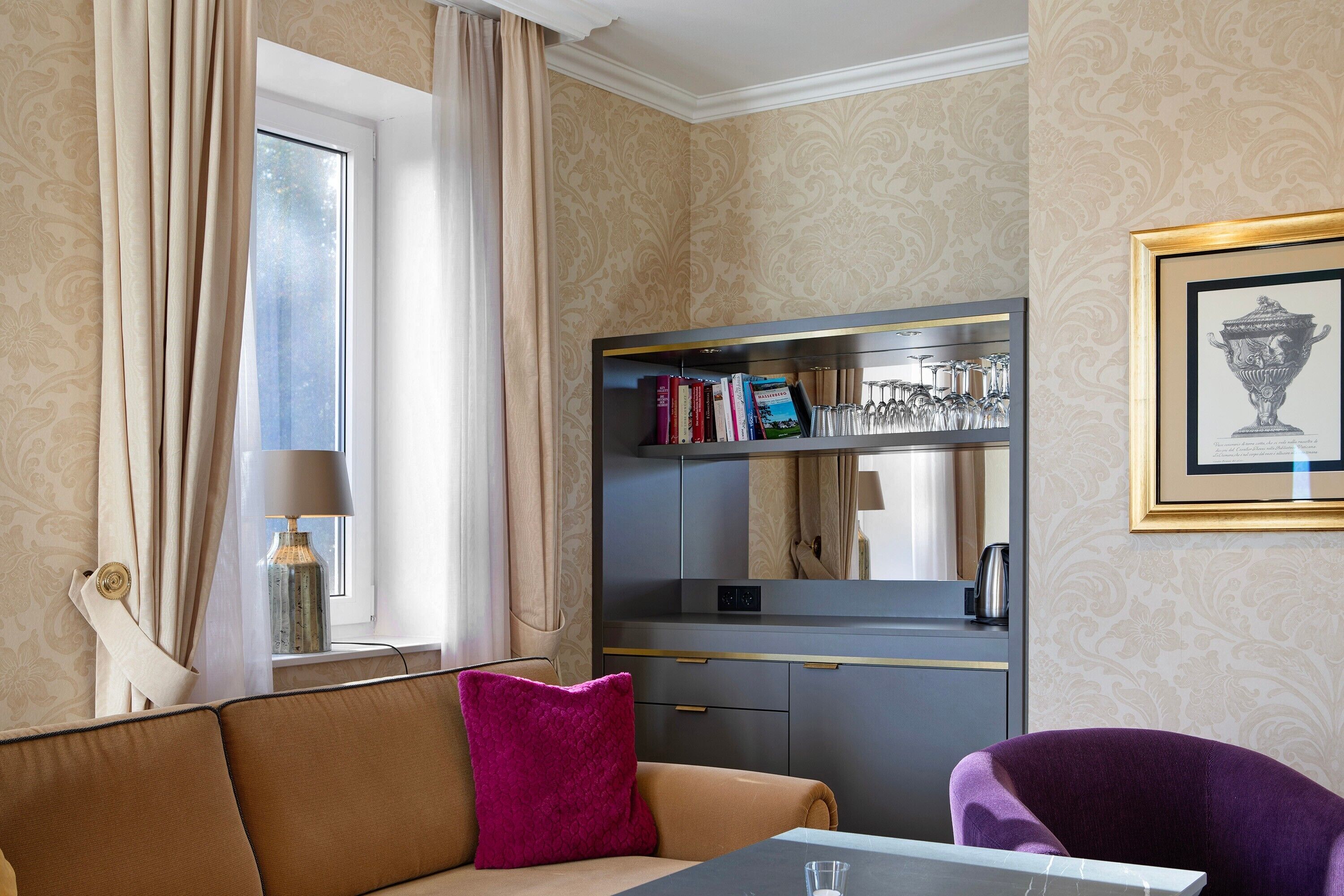 A room with a sofa, a table, a bookshelf, a window with curtains, and a framed picture on the wall.