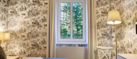 A bedroom with a bed, a chair, a lamp, and a window with a view of trees.