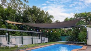 A rectangular swimming pool with a brick border, surrounded by a stone patio. There are lounge chairs and a shaded area with string lights. - Elysium Retreat & Stays (Bondoola)