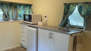 A compact kitchen with a microwave, a small refrigerator, a sink, and a window with curtains. - Elysium Retreat & Stays (Bondoola)