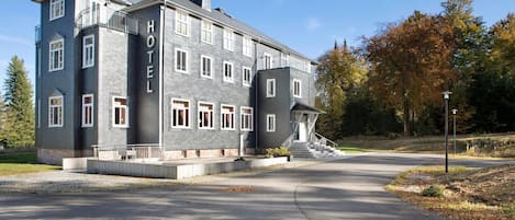 A large, multi-story hotel with a prominent 'HOTEL' sign on the facade, a central entrance with a staircase, and a driveway leading to the entrance.
