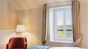 Ein Hotelzimmer mit einem Bett, einem Sessel, einer Lampe und einem Fenster mit Vorhängen.