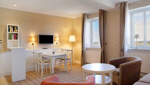 Ein Hotelzimmer mit Esstisch, Stühlen, einem Fernseher, einer kleinen Sitzecke und einem Fenster mit Vorhängen.