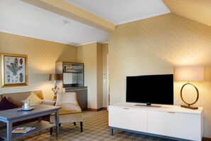Ett hotellrum med en tv, ett matbord, en soffa, en lampa och en inramad botanisk illustration.