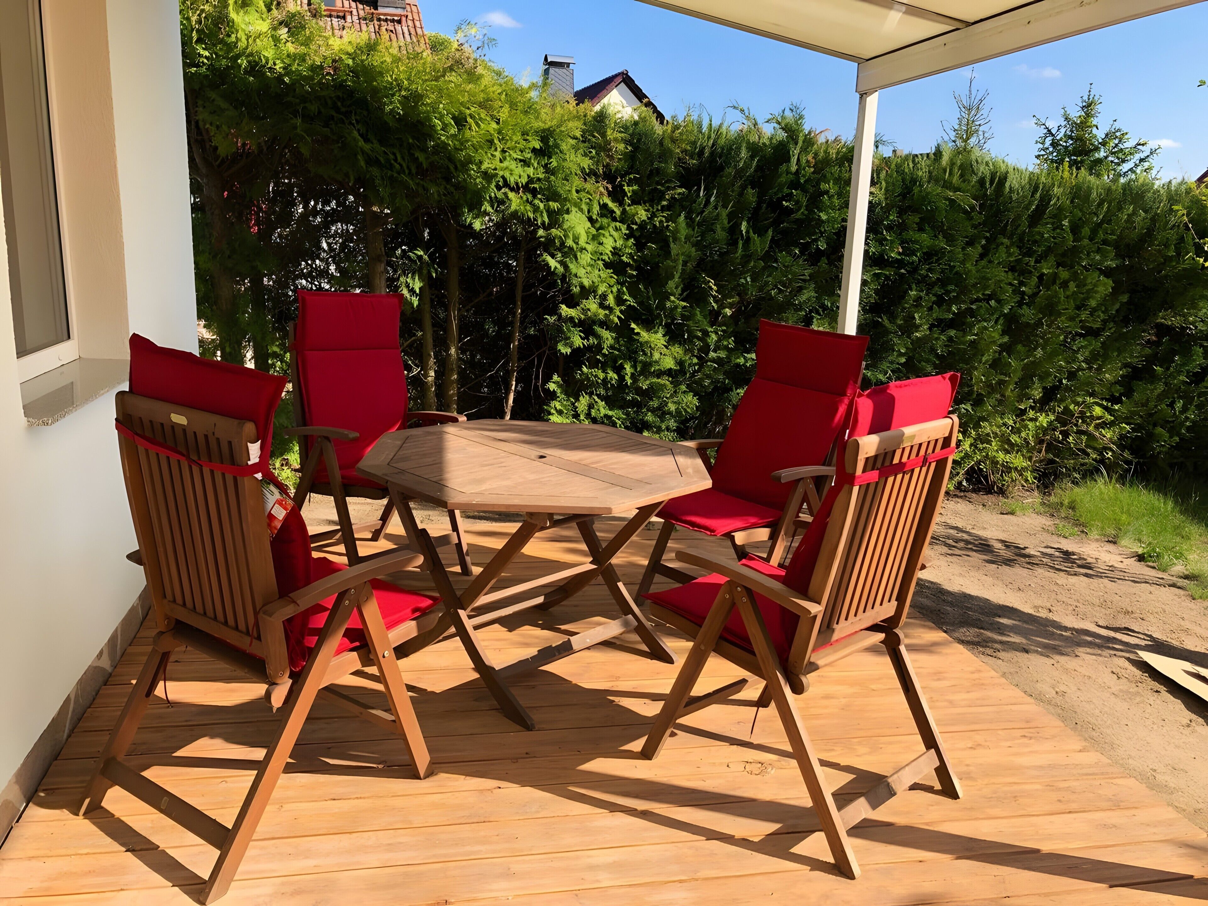 Une terrasse en bois avec une table et quatre chaises, entourée de verdure.