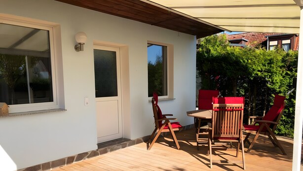 A wooden deck with a table and chairs, a door, and windows. - Apartment “Island of Relaxation Bungalow” with Private Terrace, Garden & Wi-Fi (Milmersdorf)