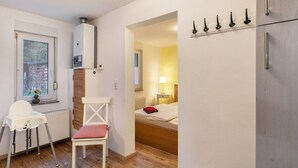 A room with a white radiator, a white chair, a bed with a red pillow, a white heater, and a wall-mounted shelf. - Apartment “Island of Relaxation Bungalow” with Private Terrace, Garden & Wi-Fi (Milmersdorf)