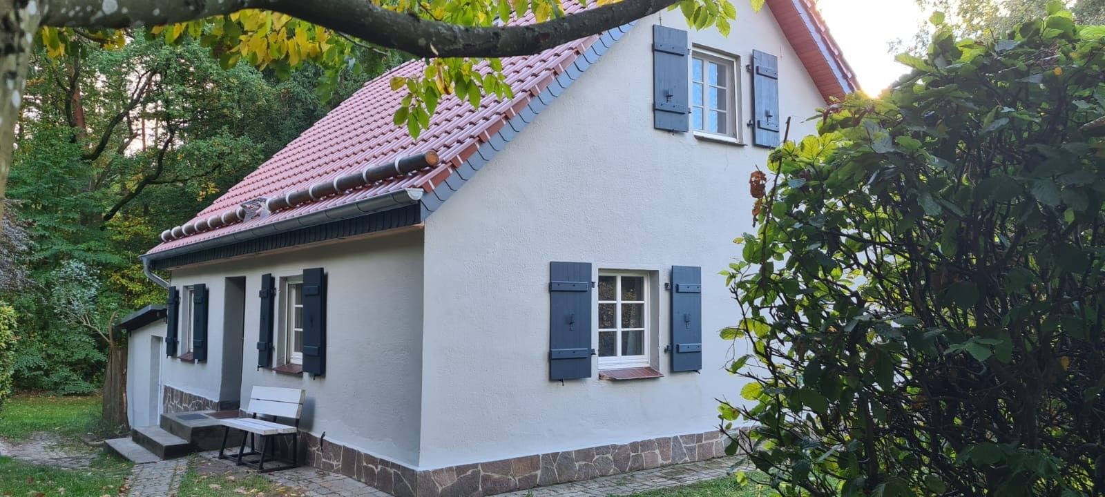 A two-story house with a red-tiled roof, white walls, and dark shutters.