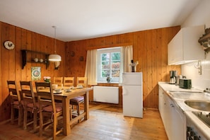 A wooden-paneled room with a dining table, chairs, a refrigerator, a sink, and a window with curtains.