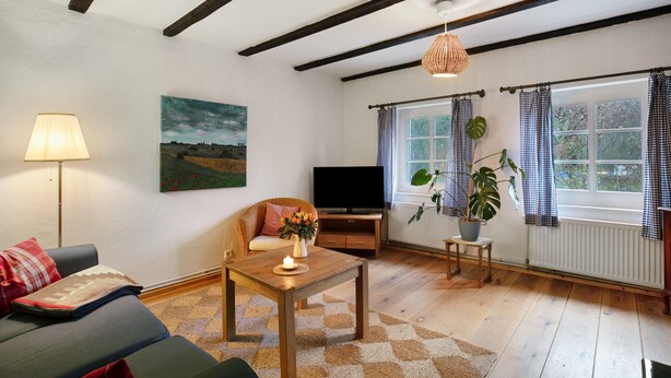 Una sala de estar con sofá, mesa, televisor, lámpara, cuadro y ventana con cortinas.