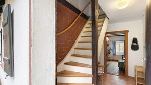 Una escalera de madera con un muro de ladrillo que lleva a una habitación con ventana y planta.