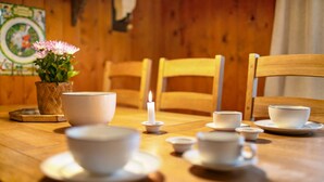 Una mesa de madera con tazas y platillos blancos, una vela encendida y un jarrón con flores.