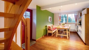 A kitchen with wooden cabinets, a dining table, and a window with curtains. - Apartment 'Haus Am See - Zur Roten Tür' with Lake View, Private Terrace and Wi-Fi (Templin)