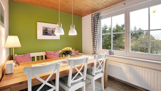 A dining area with a wooden table, white chairs, a green wall, a window with a view, and a ceiling with wooden beams. - Apartment 'Haus Am See - Zur Blauen Tür' with Lake View, Private Terrace and Wi-Fi (Templin)