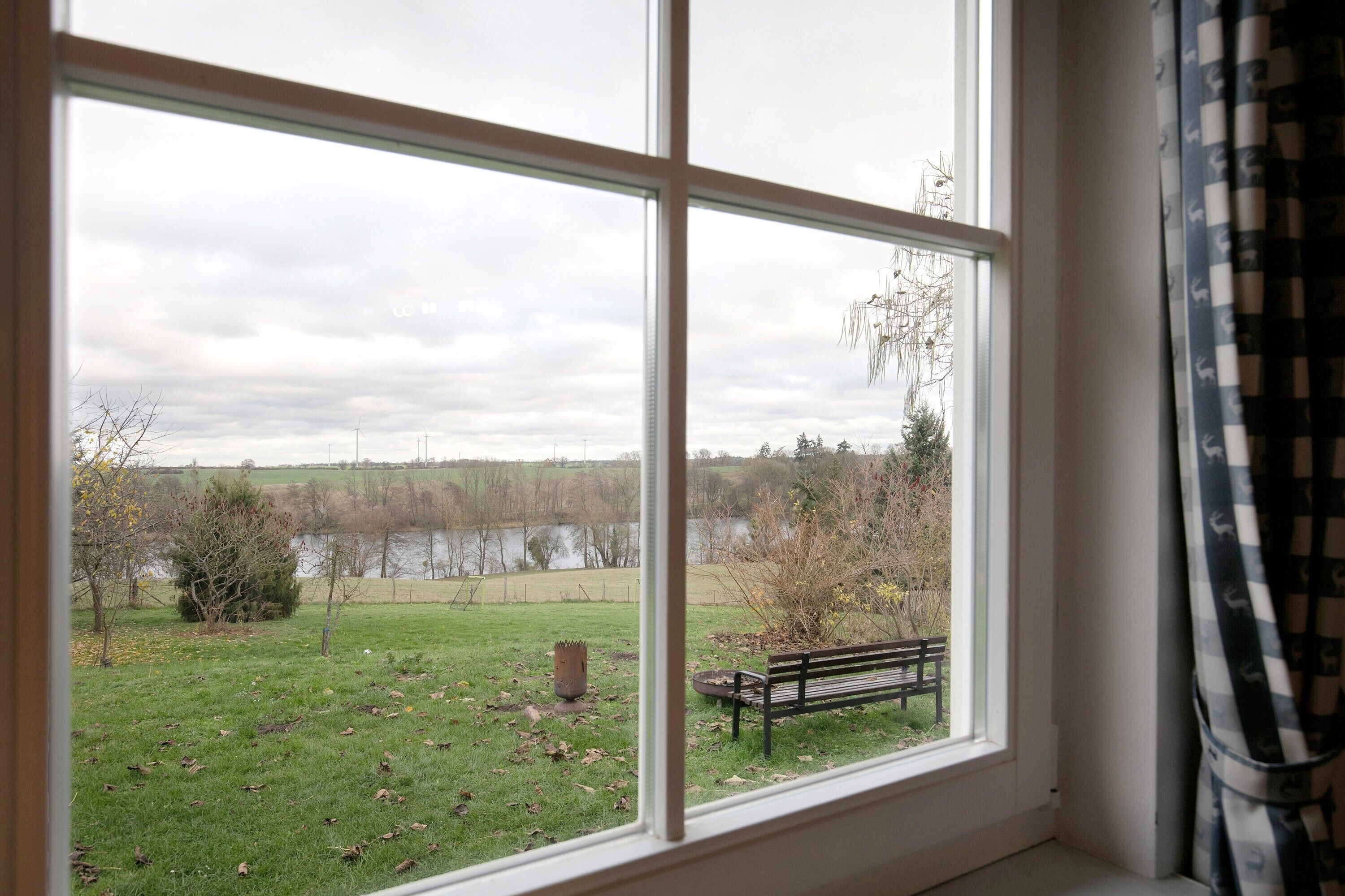 A room with a large window offering a view of a grassy area, a bench, and a body of water.