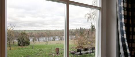 A room with a large window offering a view of a grassy area, a bench, and a body of water.