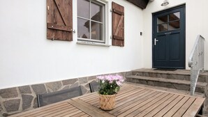 A wooden table with a woven basket of flowers, a stone wall, and a dark blue door. - Apartment 'Haus Am See - Zur Blauen Tür' with Lake View, Private Terrace and Wi-Fi (Templin)