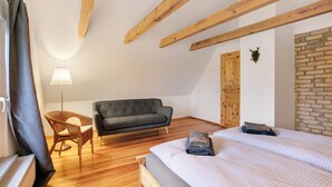 A bedroom with a bed, a sofa, a chair, wooden beams, a radiator, a lamp, and a brick wall. - Apartment 'Haus Am See - Zur Blauen Tür' with Lake View, Private Terrace and Wi-Fi (Templin)