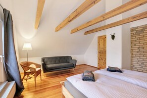 Un dormitorio con cama, sofá, sillón, vigas de madera, radiador, lámpara y pared de ladrillo.